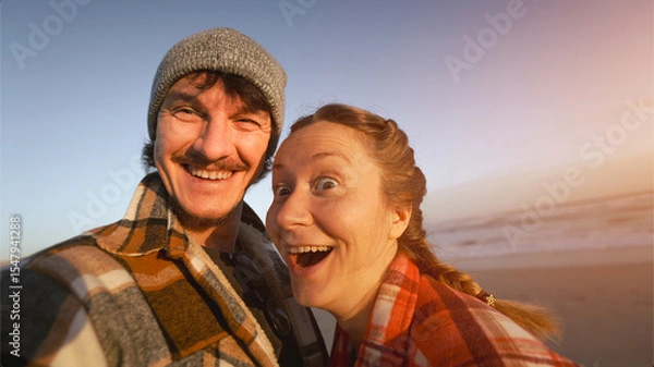 Fototapeta funny Couple in warm Plaid Shirts Embracing and Taking Selfie by the Ocean