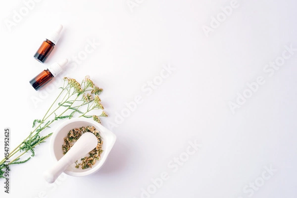Fototapeta Herbal cosmetic set with essential oil bottles, dried yarrow flowers and mortar on white background. Top view, flat lay, copy space