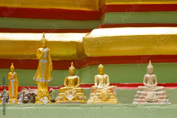 Fototapeta Small buddha icons line a shelf on a colorful green, red and gold temple stupa