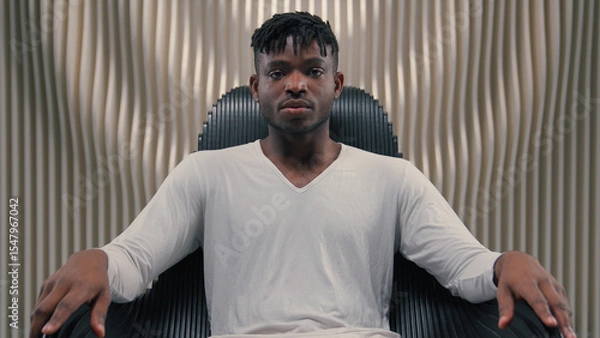 Fototapeta Futuristic confident serious gamer programmer hacker African American man guy male sitting in chair in futurism modern room studio in chair looking at camera 3D computer graphics AI network concept
