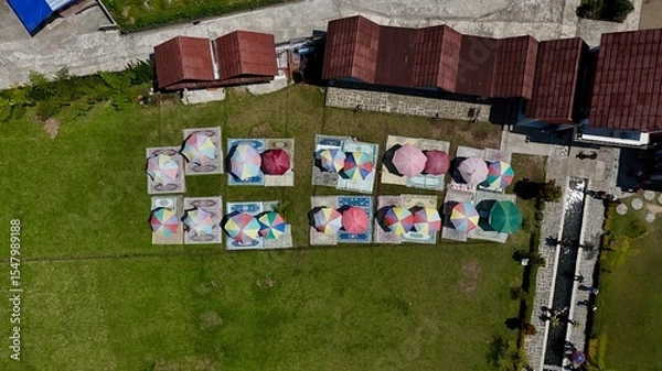 Fototapeta Vibrant top-down aerial view of colorful picnic setups with umbrellas and carpets on a manicured green lawn for outdoor leisure