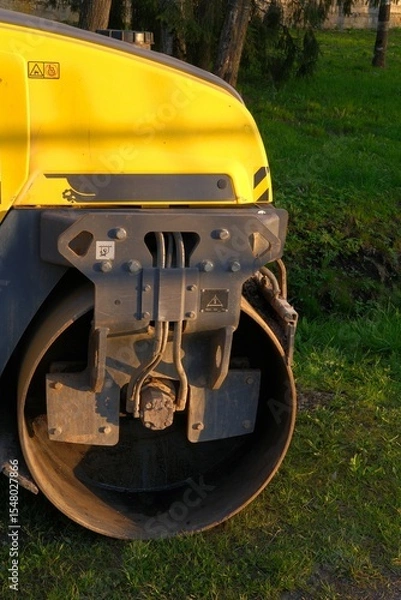 Fototapeta Yellow construction roller drum machine parked on green grass. Construction and landscaping vehicle and equipment. Compaction tasks during earthwork, landfills and agriculture maintenance
