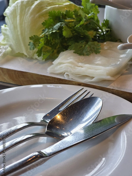Obraz Fresh herbs and cutlery arranged on plate, showcasing culinary setting with lettuce and cilantro. shiny utensils reflect light, adding touch of elegance to dining experience