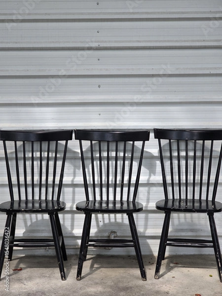Obraz Black wooden chairs arranged against metal wall, showcasing their sleek design and shadows. simplicity of chairs adds modern touch to industrial setting
