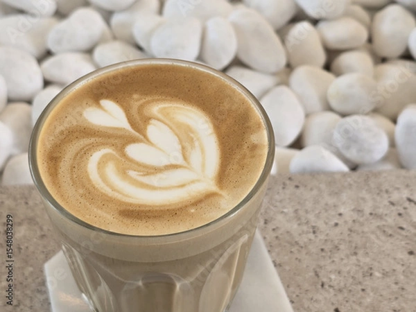 Obraz beautifully crafted latte with intricate foam art sits atop smooth surface, surrounded by white pebbles, creating serene and inviting atmosphere