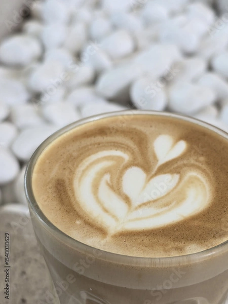 Obraz beautifully crafted latte with intricate foam art sits in glass cup, surrounded by backdrop of smooth white stones, creating serene and inviting atmosphere