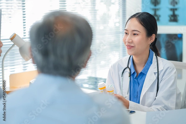 Fototapeta Asian doctor in uniform attentively assists a senior couple with medical paperwork in a hospital area, explaining health records and test results with care and professionalis senior health