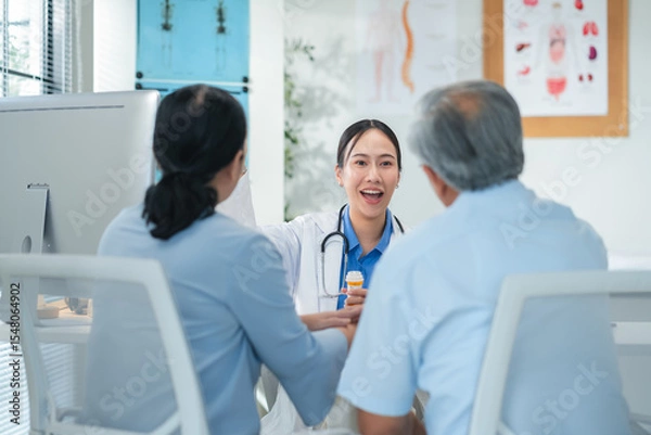 Fototapeta Asian doctor in uniform attentively assists a senior couple with medical paperwork in a hospital area, explaining health records and test results with care and professionalis senior health