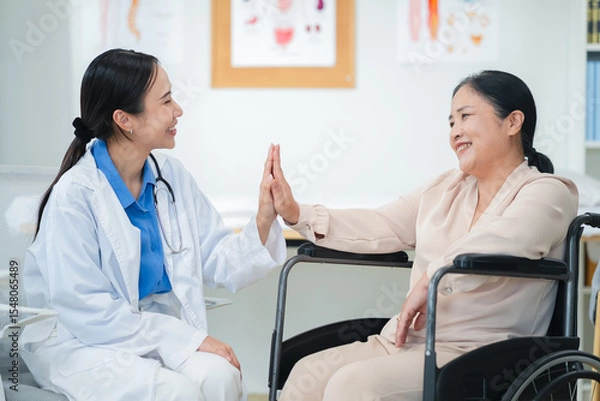 Fototapeta Asian female doctor giving a cheerful high five to an elderly woman patient, both smiling warmly in a medical clinic setting. A joyful moment of healthcare connection, trust, and support between careg