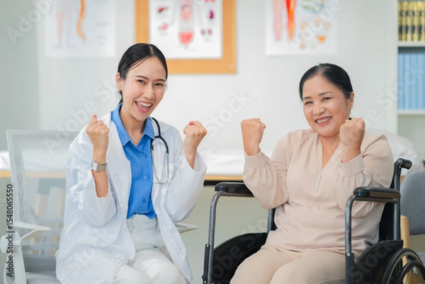 Fototapeta Asian female doctor giving a cheerful high five to an elderly woman patient, both smiling warmly in a medical clinic setting. A joyful moment of healthcare connection, trust, and support between careg