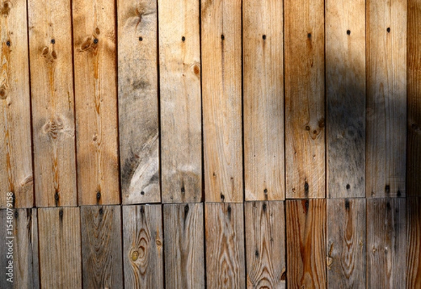 Fototapeta Vertical wooden planks create a rustic and natural appearance,with varying shades of brown and visible grain patterns.Shadow partially casts over the surface, adding depth and contrast,for copy space.