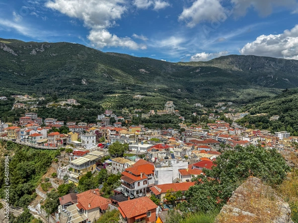 Fototapeta Panoramic view of Parga, a picturesque coastal town in Greece, famous for its colorful houses with red-tiled roofs nestled in a lush green mountain valley.