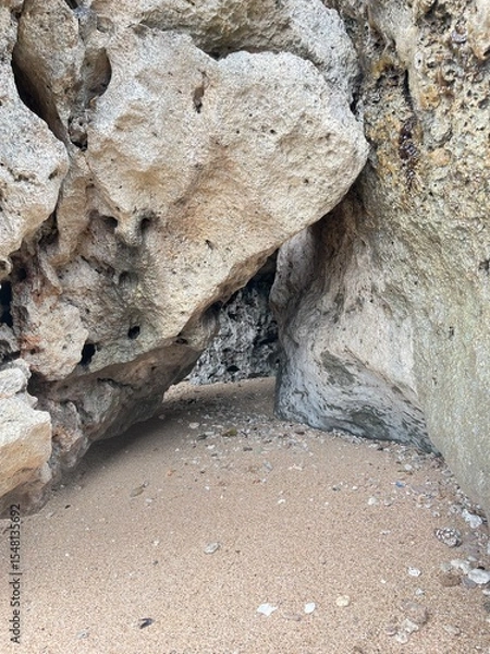 Obraz Coastal Cave: An evocative composition of weathered rocks, shaped by the sea's embrace, framing a shadowed cavern entrance and textured sand