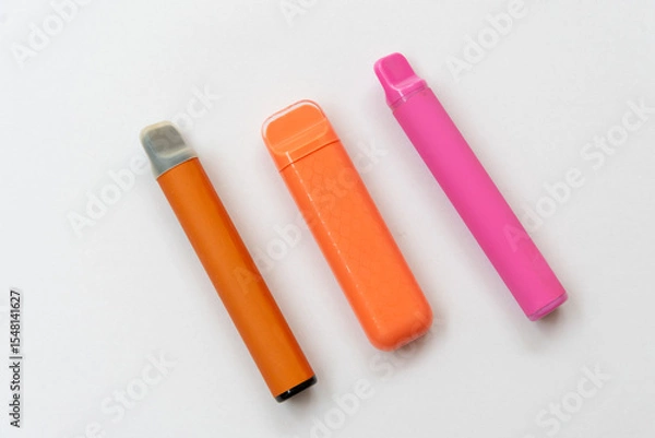 Obraz Three disposable electronic cigarettes in bright colors on a white background. Modern vape devices lying in a row.