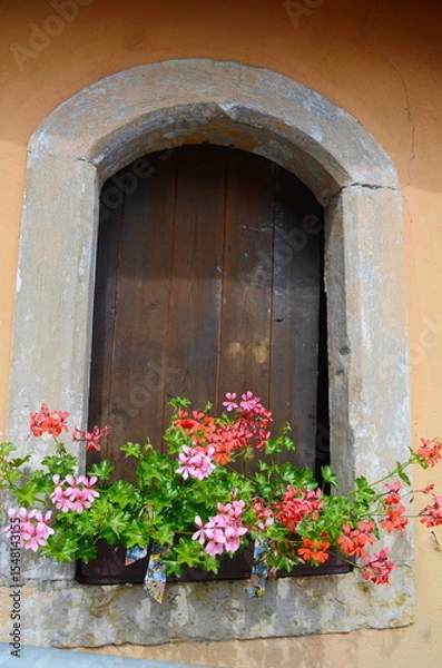 Fototapeta A bright red geranium in a clay pot in a window framed by a beautiful. weathered, thick stone wall.