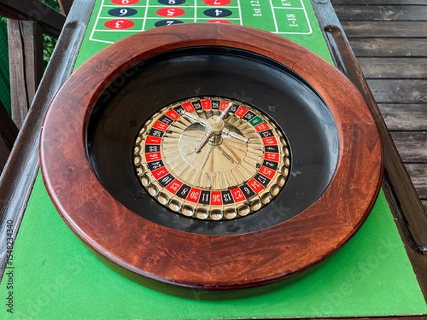 Obraz A beautifully crafted wooden roulette wheel is prominently placed on a vibrant green mat, ready to engage players in exciting games of chance and strategy, reminiscent of lively casinos