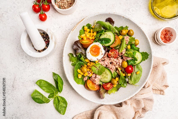 Fototapeta Tuna salad with tomatoes, cucumber, corn, olives , eggs and onion on white stone background, top view. High quality photo