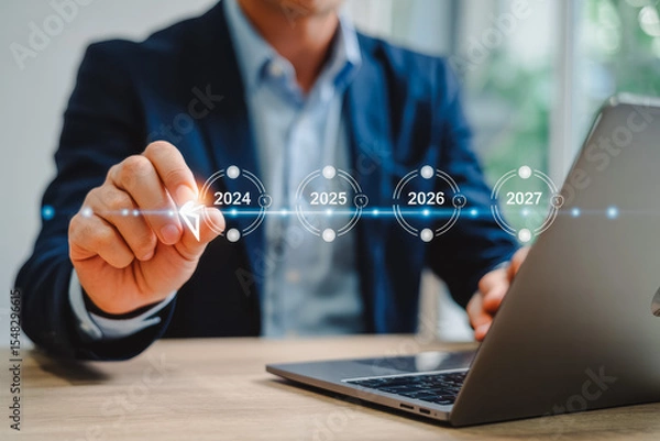 Obraz A business professional interacts with a futuristic timeline on a digital screen, highlighting the years 2024, 2025, 2026 to 2027. This symbolizes innovation and strategic planning using technology.
