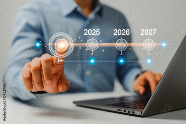 Obraz A person interacts with a digital timeline projected above a laptop, highlighting future years 2025, 2026 to 2027, symbolizing business planning and strategic foresight in technology.