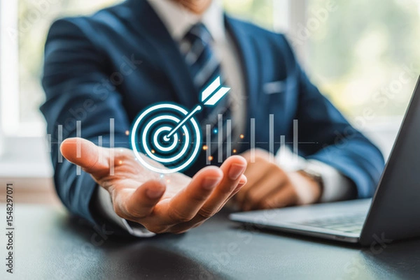 Obraz A businessman holds a glowing target icon, symbolizing precision and goal achievement. Next to him, a laptop reflects modern technology and innovation. Ideal for business success concepts.
