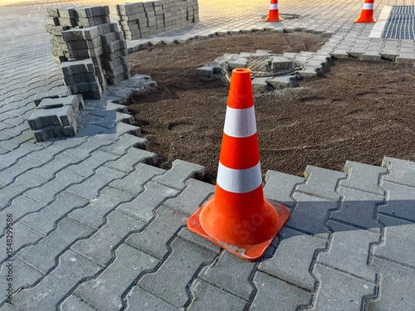 Fototapeta Traffic cones indicate ongoing construction work on a stone pavement. Workers reshape the area, adjusting materials and ensuring public safety during the day