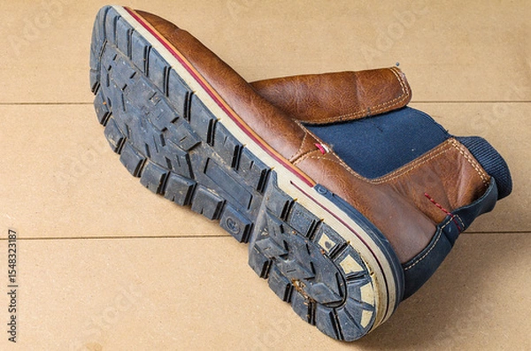 Fototapeta Worn black leather men’s shoe with visible sole placed on wooden surface background