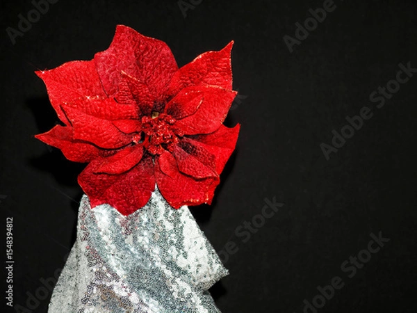 Fototapeta Glamor red flower on stand wrapped in silver cloth with glitter. Dark background. Minimalistic still life. Copy space