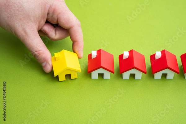 Fototapeta The hand places the yellow house in a row with the others. A unique offer. Milestone achieved through the sale or construction of real estate. Project completion. Importance of choosing the right home