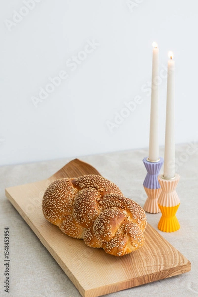 Fototapeta sesame seed challah bread on wooden board on table with two shabbat candles in colorful holders
