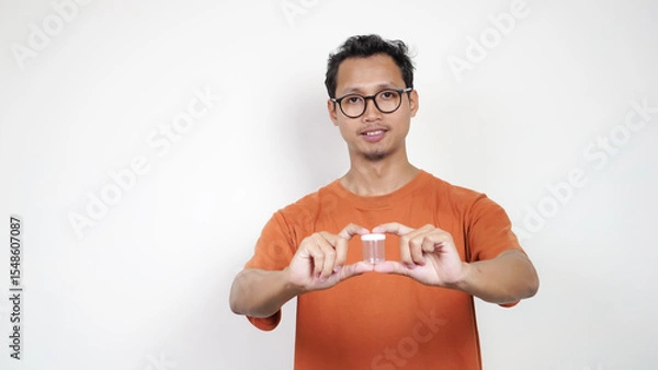 Obraz A man in an orange shirt is holding a clear container
