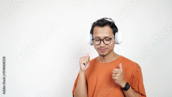 Obraz A man in an orange shirt is wearing headphones and talking on a cell phone