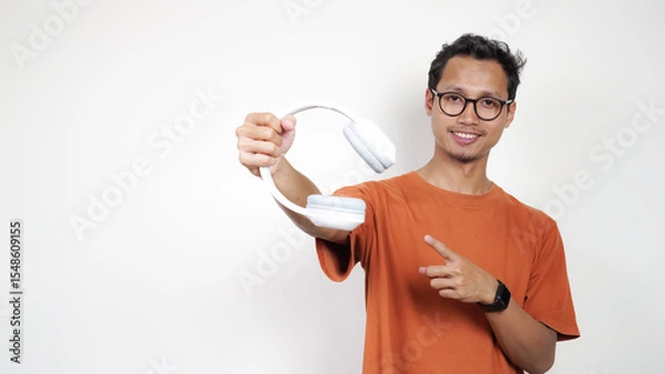 Obraz A man in an orange shirt is holding a white earbud and pointing to it