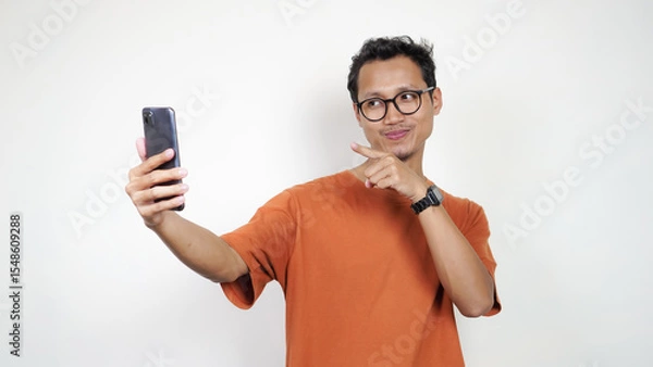 Obraz A man in an orange shirt is taking a picture of himself with his cell phone