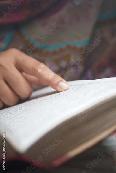 Fototapeta Person reading a quran while pointing to the text