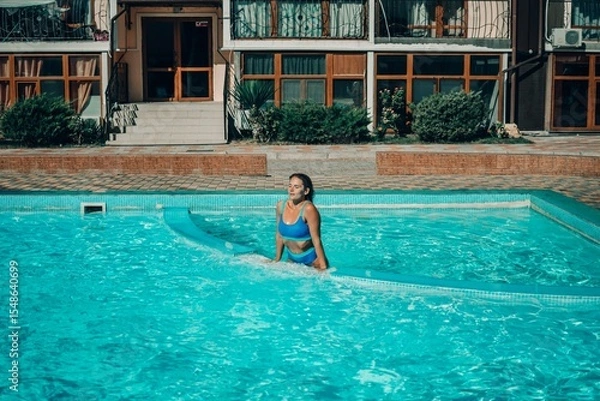 Obraz A woman is in the water, smiling and enjoying herself. The water is blue and the pool is surrounded by a white ledge.
