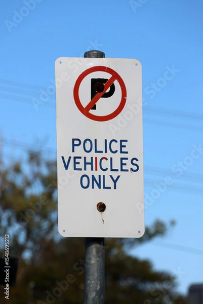 Fototapeta Police Vehicles Only parking sign mounted on a metal pole with a tree and blue sky in the background