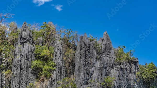 Fototapeta Steep karst cliffs against a background of blue sky and clouds. There is green tropical vegetation on the steep, furrowed slopes. Philippines. Palawan.