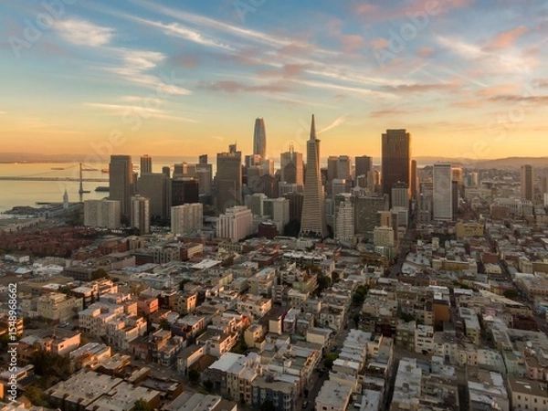 Fototapeta Aerial view of San Francisco, California, USA, at sunset. The photo shows the city skyline, including the Transamerica Pyramid and Salesforce Tower. The Bay Bridge is visible in the distance.