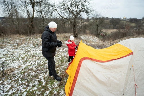 Fototapeta Camping adventure with family in winter landscape creating lasting memories near the fields while setting up a cozy tent in the chilly atmosphere