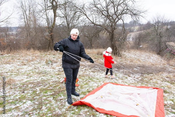 Fototapeta Setting up a winter camping tent on a snowy hillside with family enjoying quality time outdoors in a serene landscape