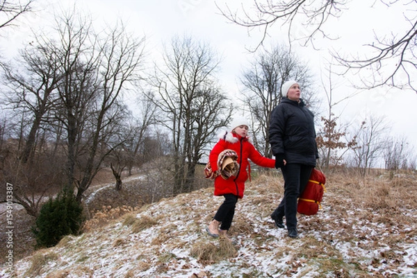 Fototapeta Winter walk with child in red coat exploring snowy landscape near trees during overcast weather in early afternoon