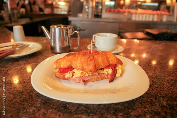 Fototapeta Plate of savoury breakfast croissant with scrambled eggs ham cheese tomato bacon in a cozy diner setting cafe setting. Shot in famous restaurant cafe in Asunción, Paraguay. Desayuno. Selective focus.