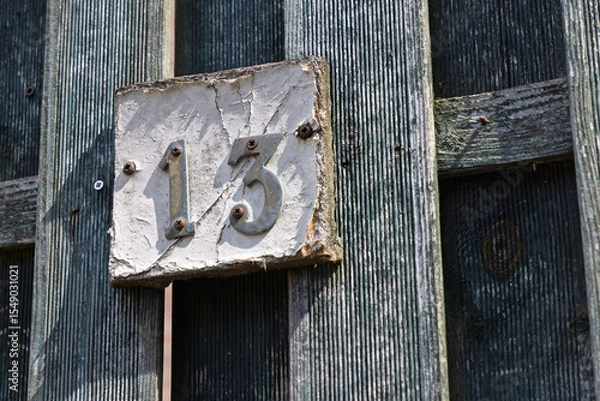 Obraz A rustic, weathered house number '13' on a distressed wooden fence, full of character.