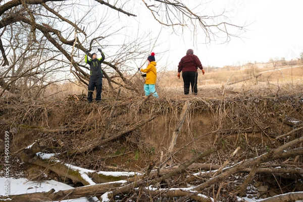 Fototapeta Exploring the riverside in wintertime as three friends enjoy nature and camaraderie during a chilly afternoon adventure in the countryside