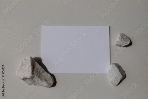 Fototapeta Empty card with white decorated stones and sunlight shadows on neutral background. Aesthetic composition for minimalistic template in flat lay style.