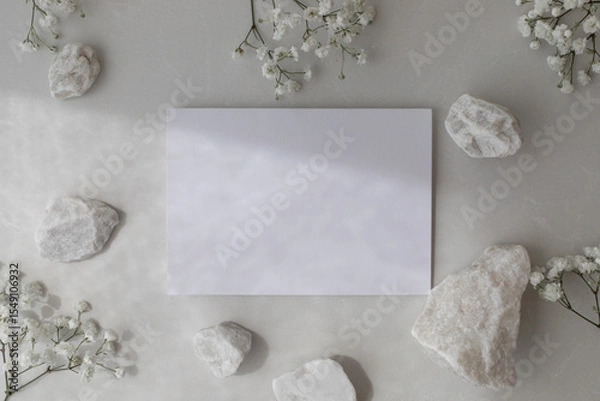 Fototapeta Neutral background with white decorated stones, blank paper card and gypsophila flowers in flat lay style. Spa or wedding invitation in minimalistic modern style.