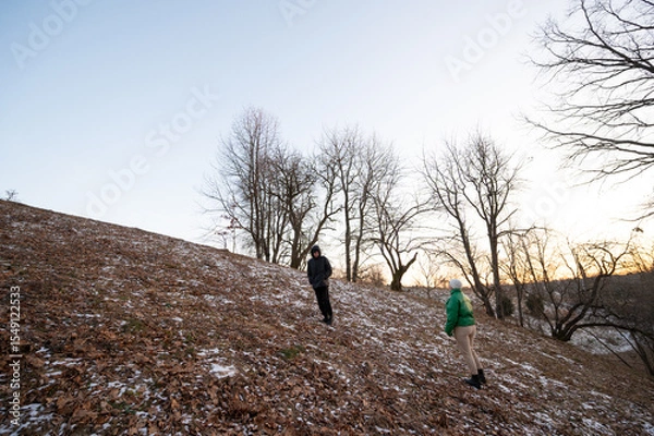 Fototapeta Exploring the serene winter landscape at dusk, two figures navigate a snow dusted hillside under the fading light of day
