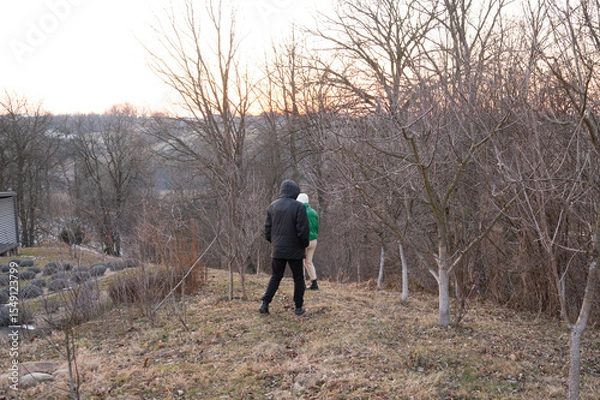 Fototapeta Strolling through a winter landscape at dusk near a hillside orchard with two figures exploring nature's beauty