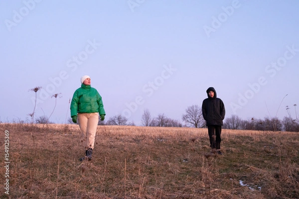 Fototapeta Twilight stroll across an open field with friends enjoying nature's tranquility and warm attire in early evening light, embracing the serene moment together