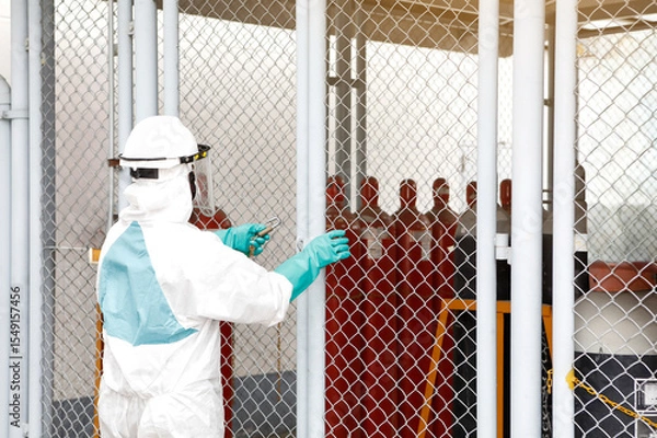 Obraz Worker in PPE Handling Gas Cylinders Behind Safety Barrier